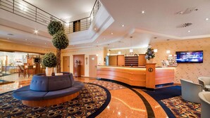 A modern hotel lobby with a reception desk, seating area, and a large TV screen. - Hotel Partner (Warsaw)