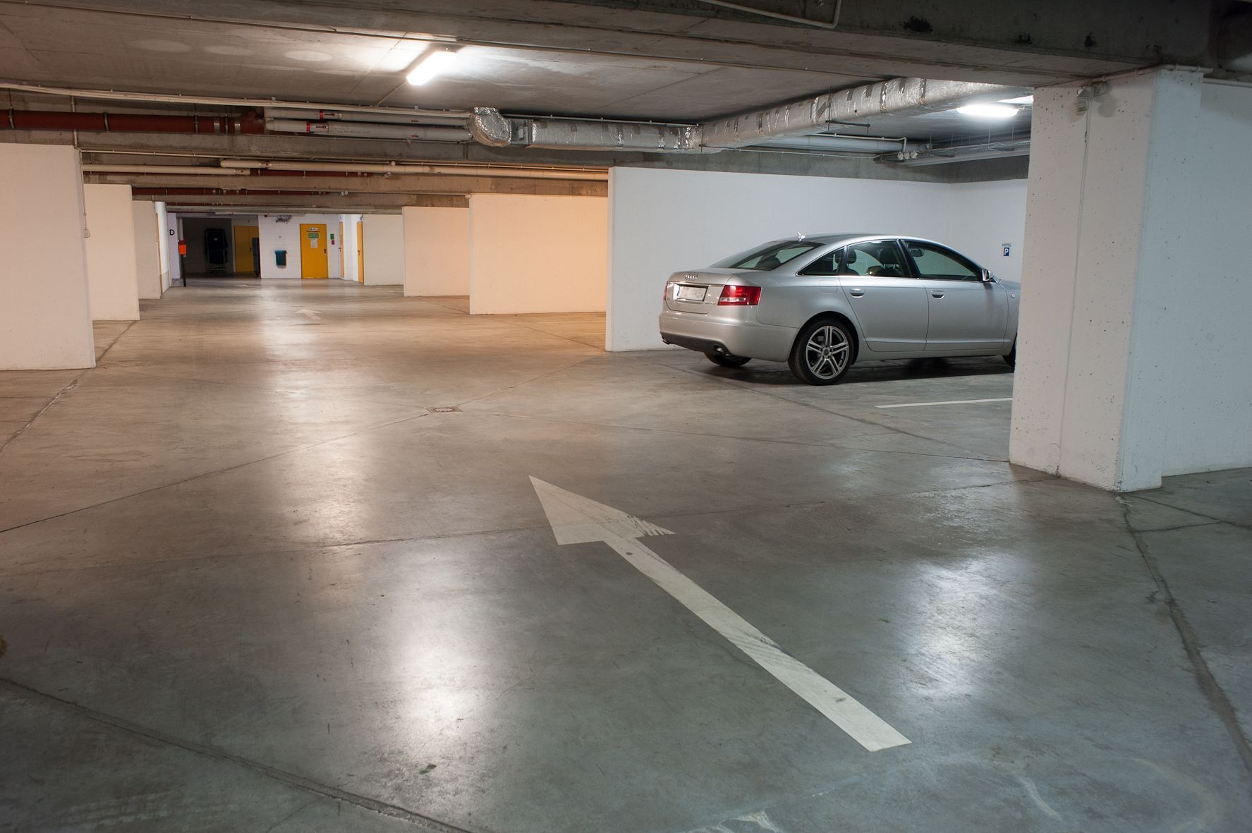 A parking garage with a car parked in a spot, concrete floors, and directional arrows on the ground.