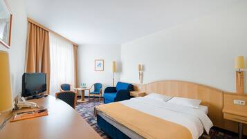 Habitación de hotel con cama, escritorio con computadora, silla, mesita de noche con lámpara y televisión.