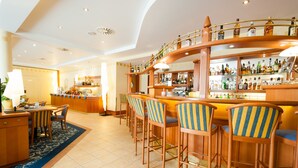A bar area with wooden bar stools, a counter with a variety of bottles, and a seating area with a table and chairs. - Hotel Partner (Warsaw)