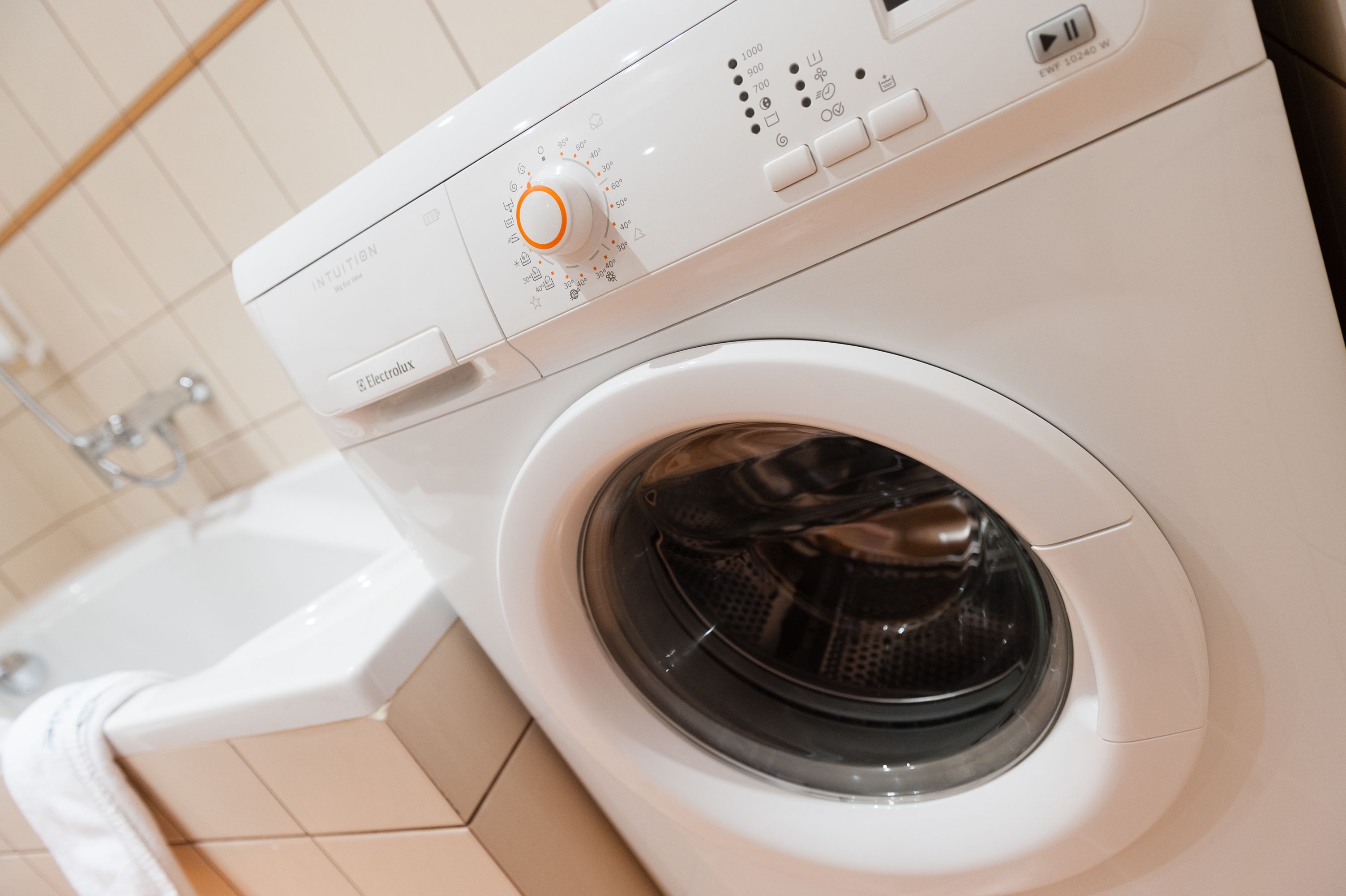A front-loading washing machine with a control panel, a tub, and a wall-mounted faucet.