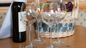 A bottle of wine, three wine glasses, and a basket with grapes and other fruits on a wooden table in a kitchen. - Hotel Partner (Warsaw)