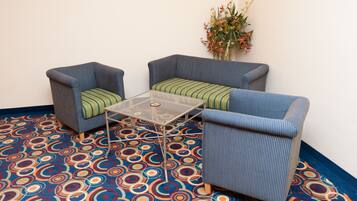 Une pièce comprenant deux fauteuils et une table basse en verre, un tapis à motifs et une composition florale accrochée au mur.