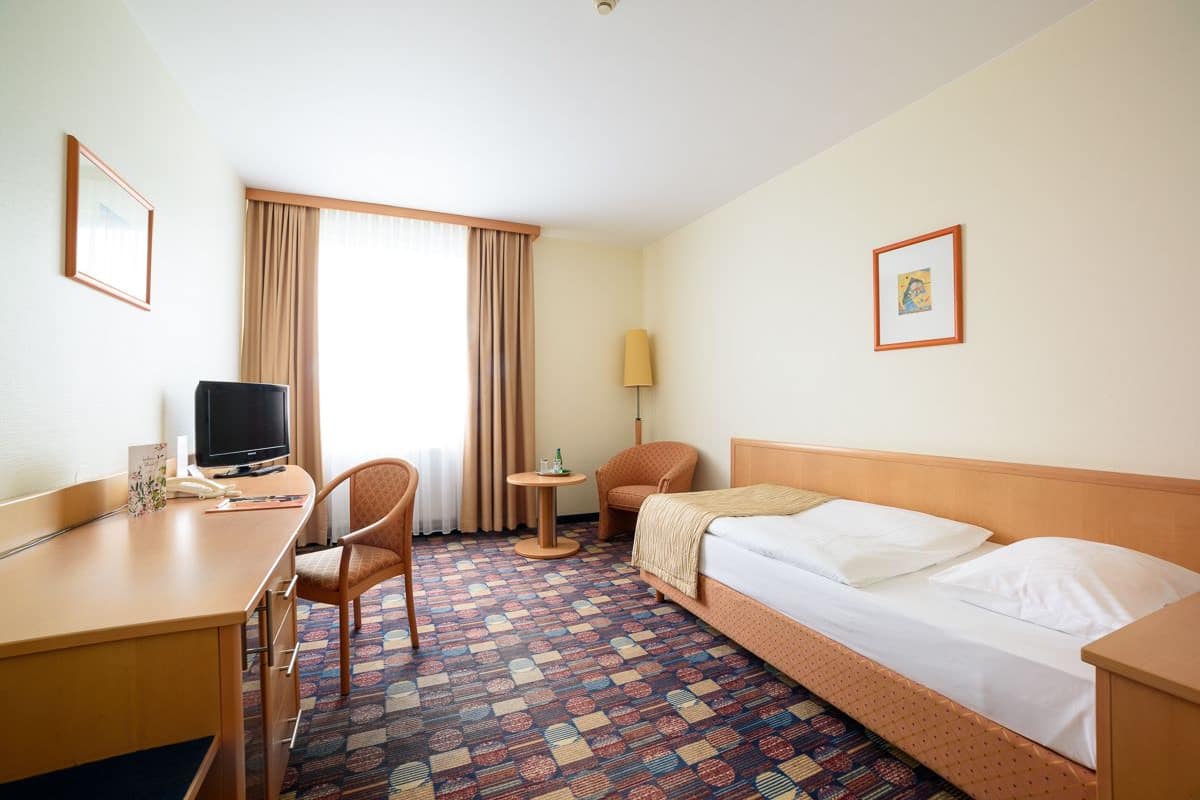 Una habitación de hotel con cama, escritorio, silla, televisor y lámpara.