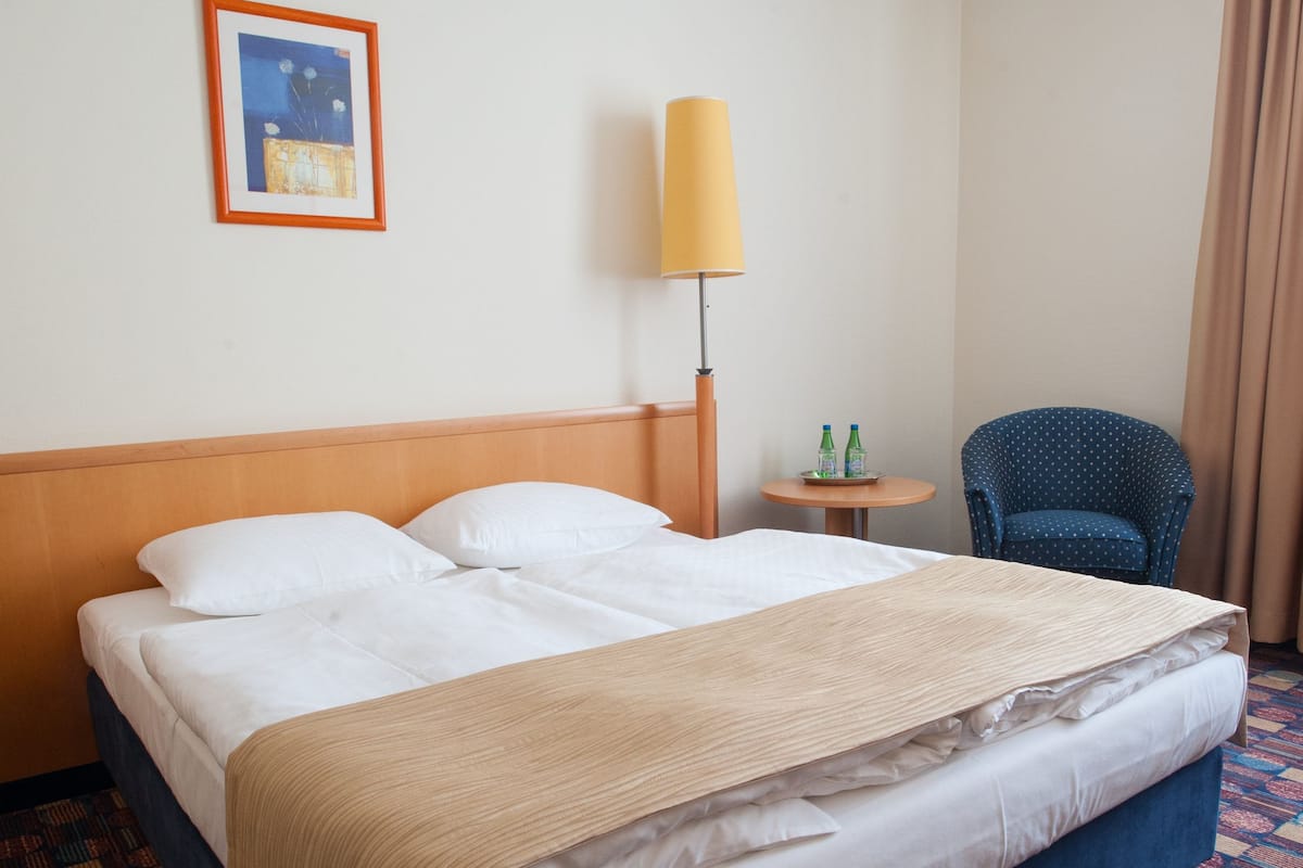 Habitación de hotel con una cama grande, una silla, una lámpara y una mesita con botellas.