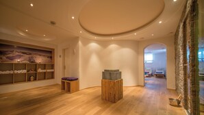 Ruime kamer met houten vloer, een houten bankje, een stenen sculptuur en een wand met handdoekenplanken.