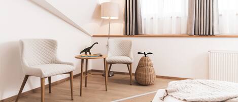 A modern bedroom with a bed, two chairs, a small table, a lamp, and a window with curtains.
