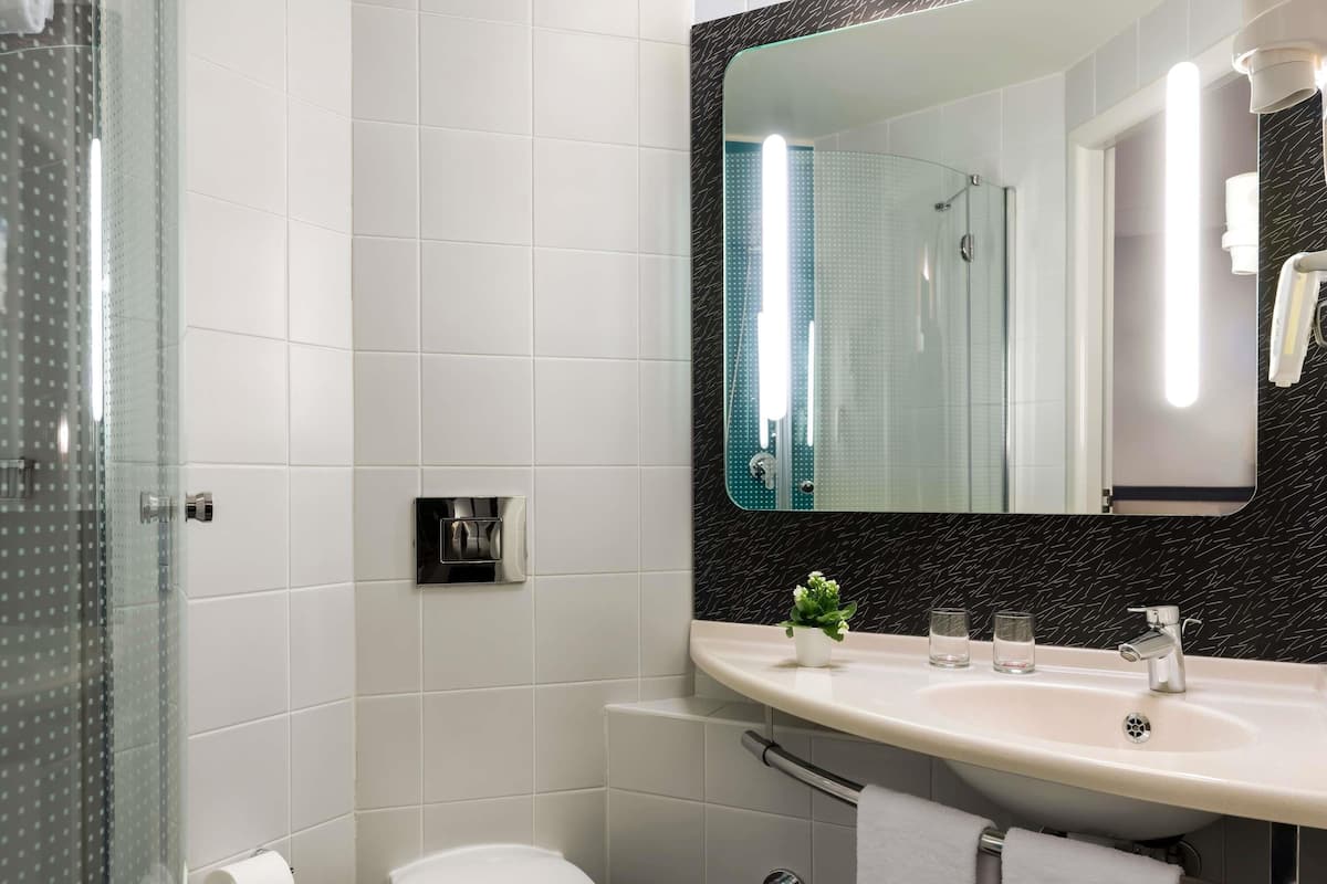 A modern bathroom with a glass shower enclosure, a toilet, a sink with a mirror above it, and a small potted plant on the sink counter.