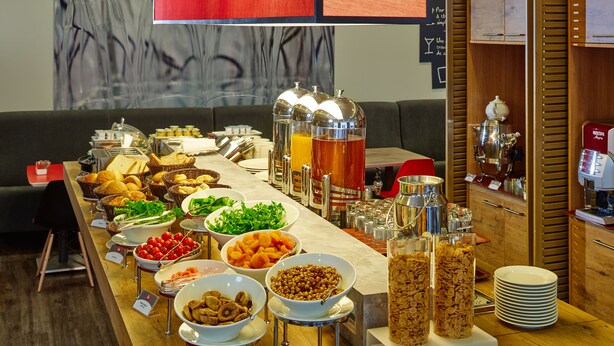 Een buffet met diverse etenswaren en drankjes, een koffieapparaat en een houten kast met keukengerei.