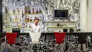 Un espace bar avec un barman, des étagères remplies de bouteilles d’alcool et une fresque murale en noir et blanc.