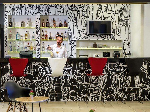 A bar area with a bartender, shelves of liquor, and a black and white mural on the wall. - Hotel ibis Ankara Airport (Akyurt)