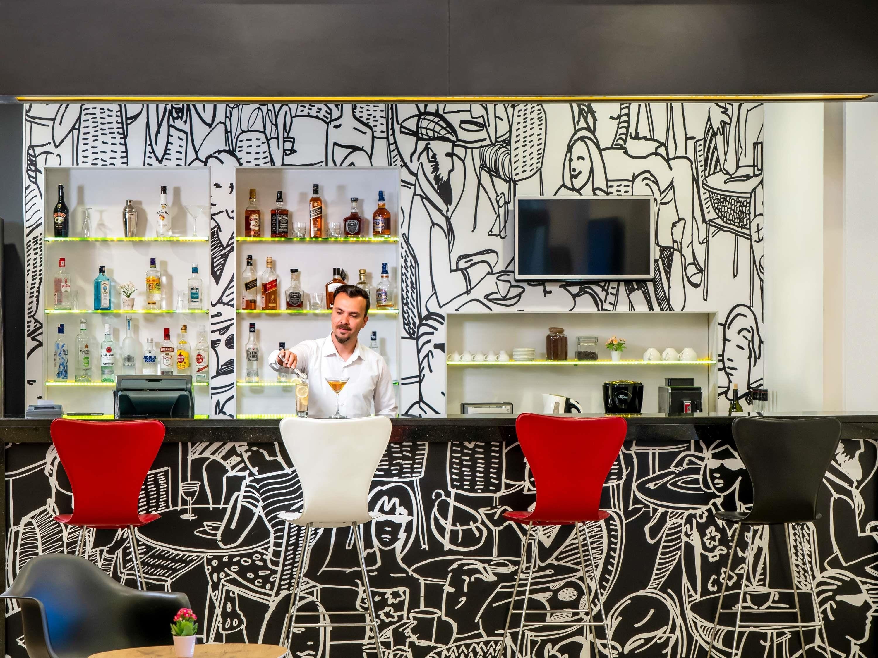 A bar area with shelves of liquor bottles, a TV mounted on the wall, and a counter with a person behind it.