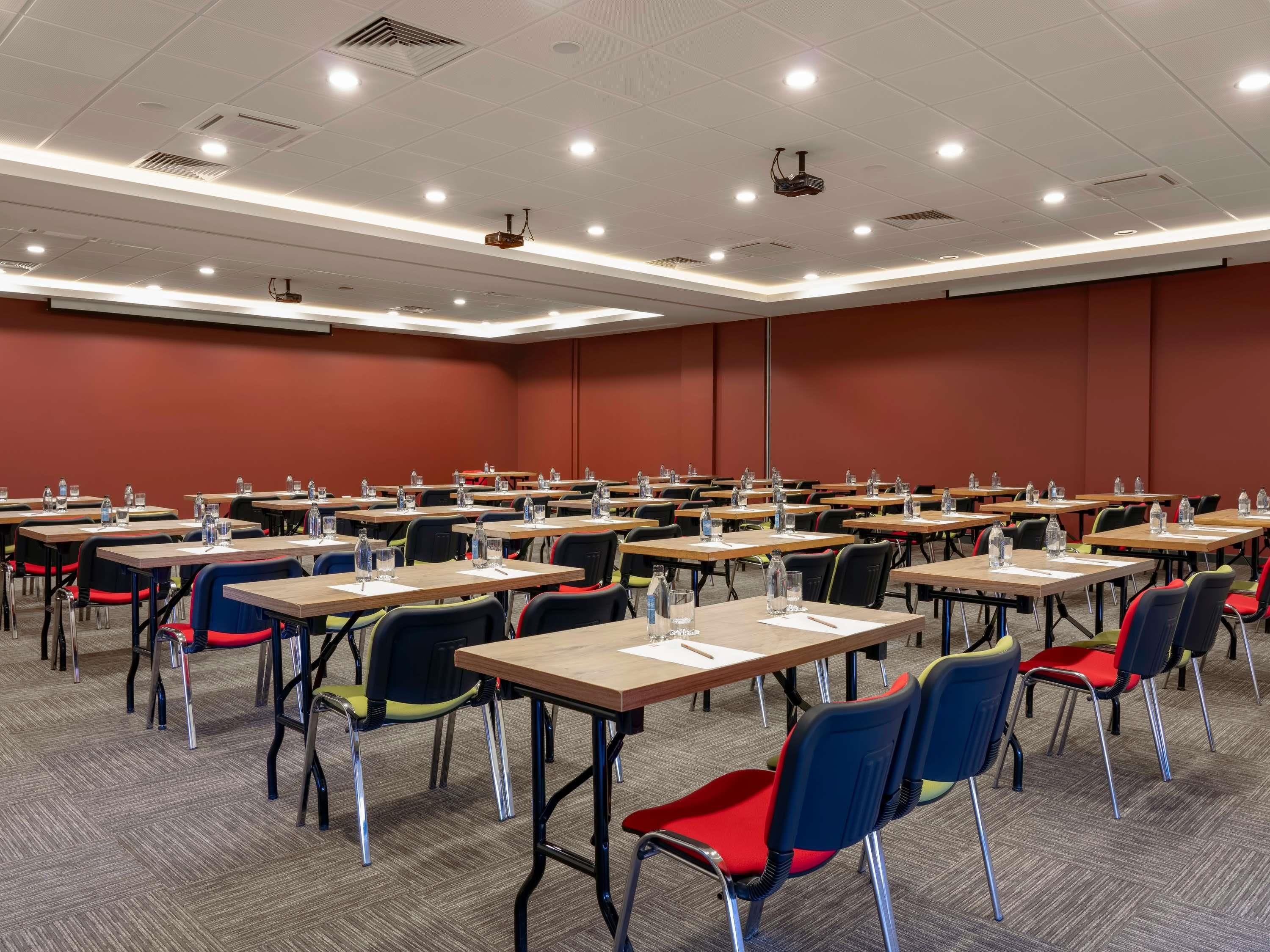 A conference room with multiple tables and chairs, equipped with water bottles and papers.