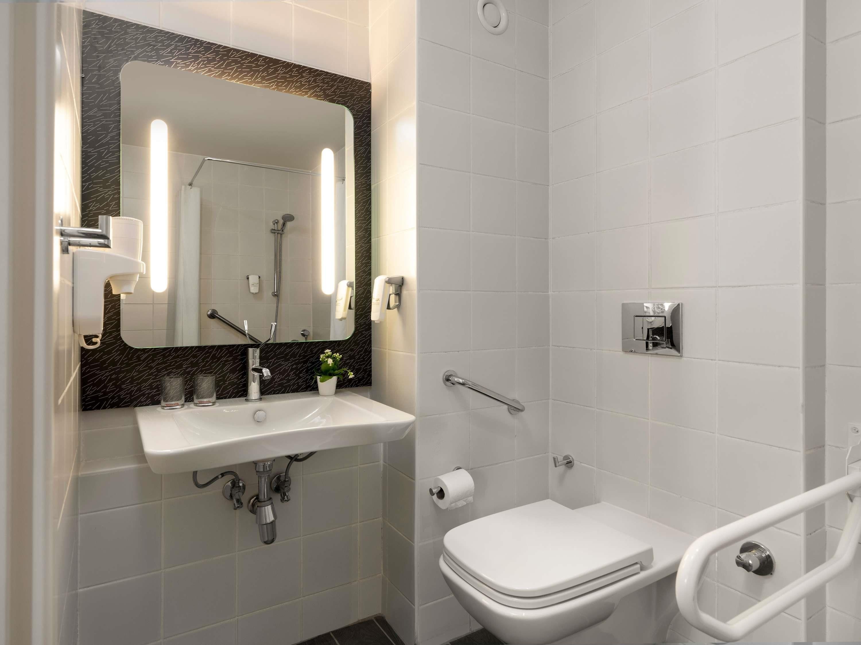 Een moderne badkamer met een wit wastafel, spiegel en toilet, voorzien van een handdouche en handgrepen.