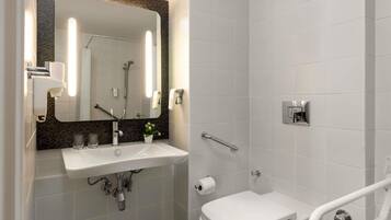 Een moderne badkamer met een wit wastafel, spiegel en toilet, voorzien van een handdouche en handgrepen.