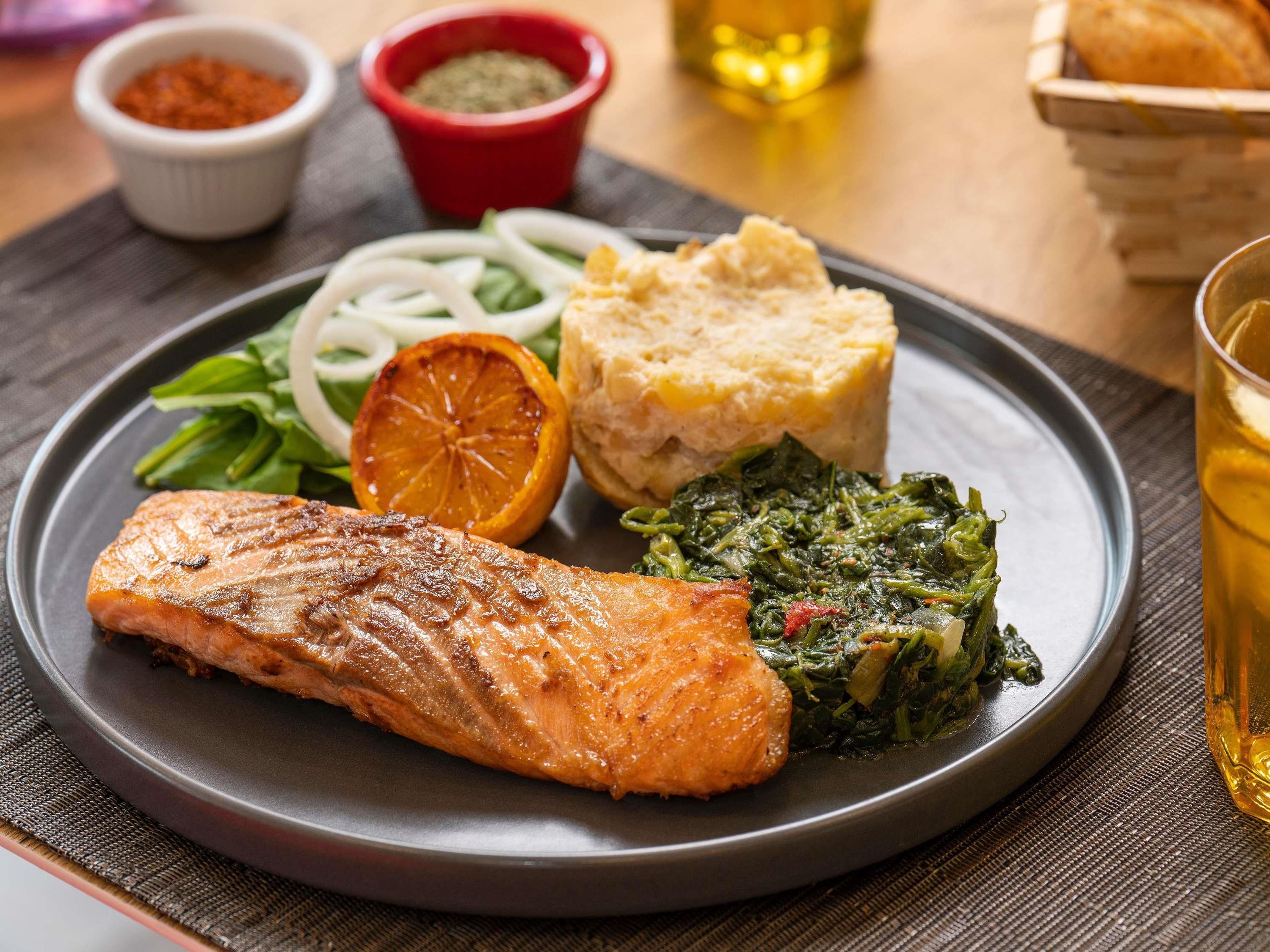 A plate with grilled salmon, greens, and a side of bread.