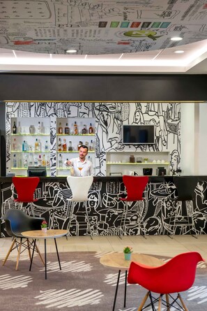 A bar area with a bartender, shelves of liquor, and a mural with abstract designs.