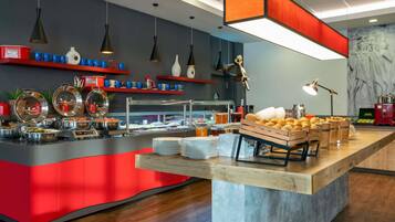 A modern breakfast bar with a red and grey color scheme, equipped with various breakfast items and a coffee station.