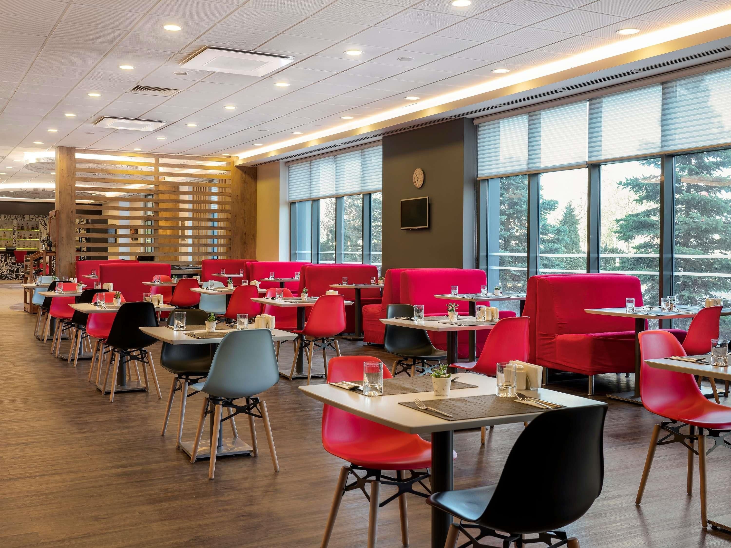 A modern restaurant with red booths and black chairs, large windows, and a wooden floor.
