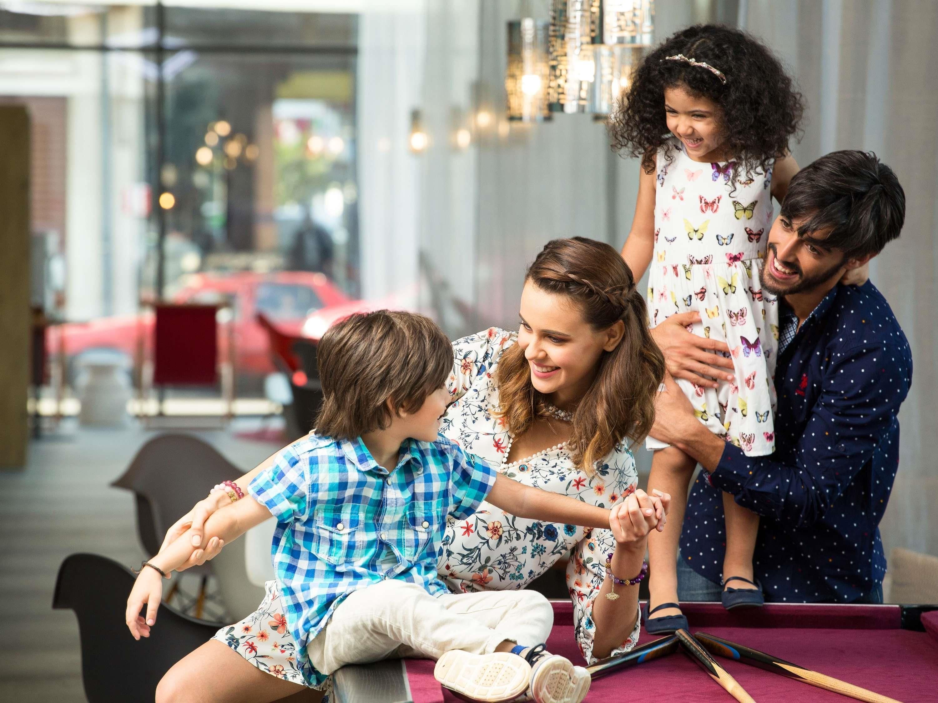 A family of four seated at a pool table in a well-lit indoor setting with a view of the street outside.