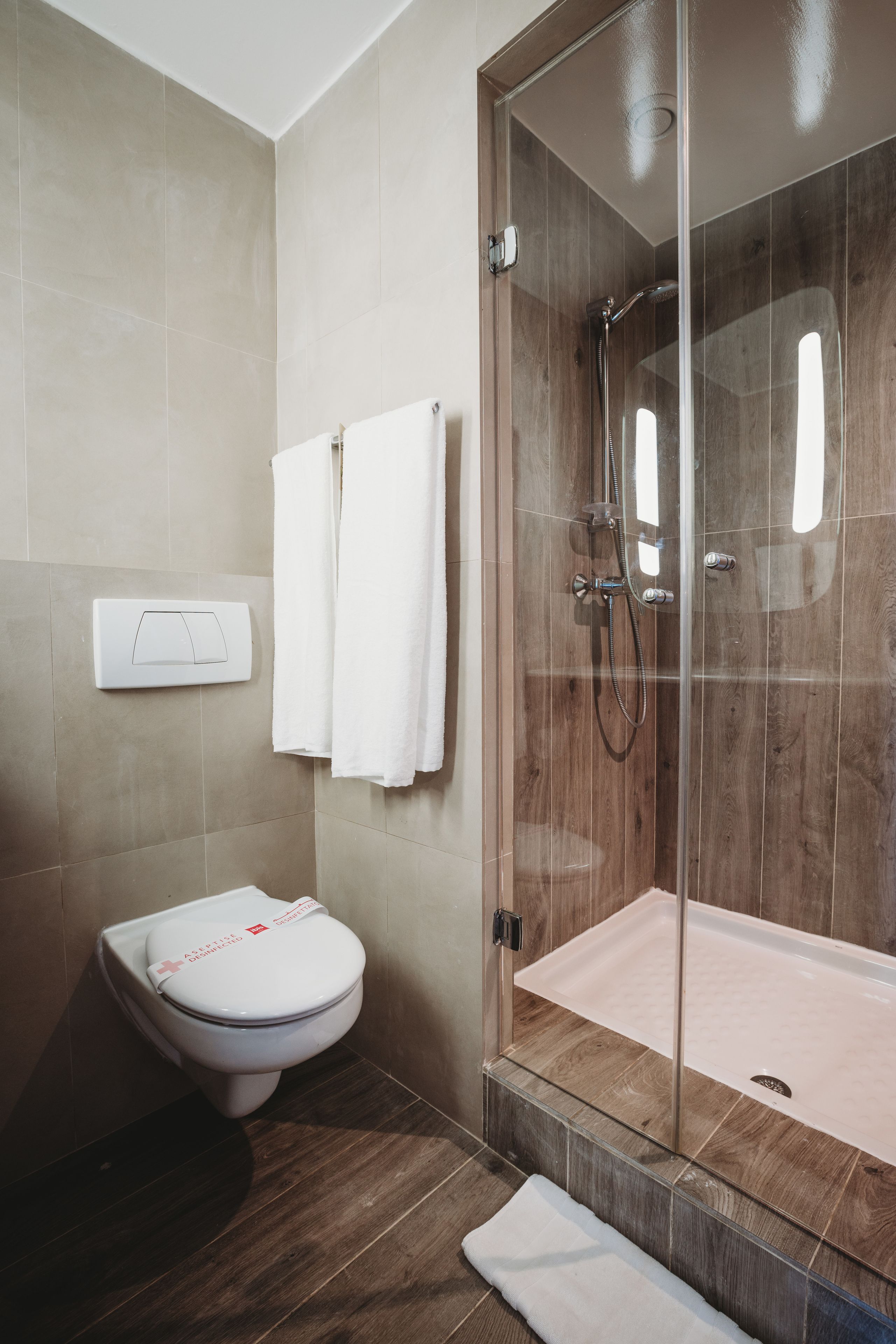 Une salle de bain avec des toilettes, une douche à parois de verre et deux serviettes blanches accrochées au mur.
