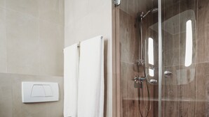 Un baño con inodoro, ducha con mampara de vidrio y dos toallas blancas colgadas en la pared.