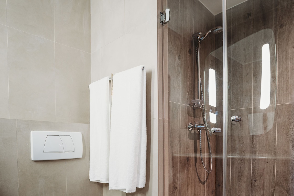 Een badkamer met een toilet, een douchecabine van glas en twee witte handdoeken aan de muur.