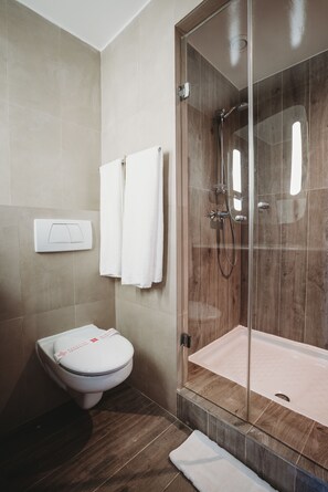 Een badkamer met een toilet, een douchecabine van glas en twee witte handdoeken aan de muur.