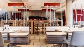 Ein modernes Restaurant mit Holztischen und -bänken, einer zentralen Bar und einer Speisekarte.