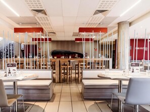 A modern restaurant interior with wooden tables and benches, a central bar area, and a menu display. - Ibis Casablanca Nearshore (Casablanca)