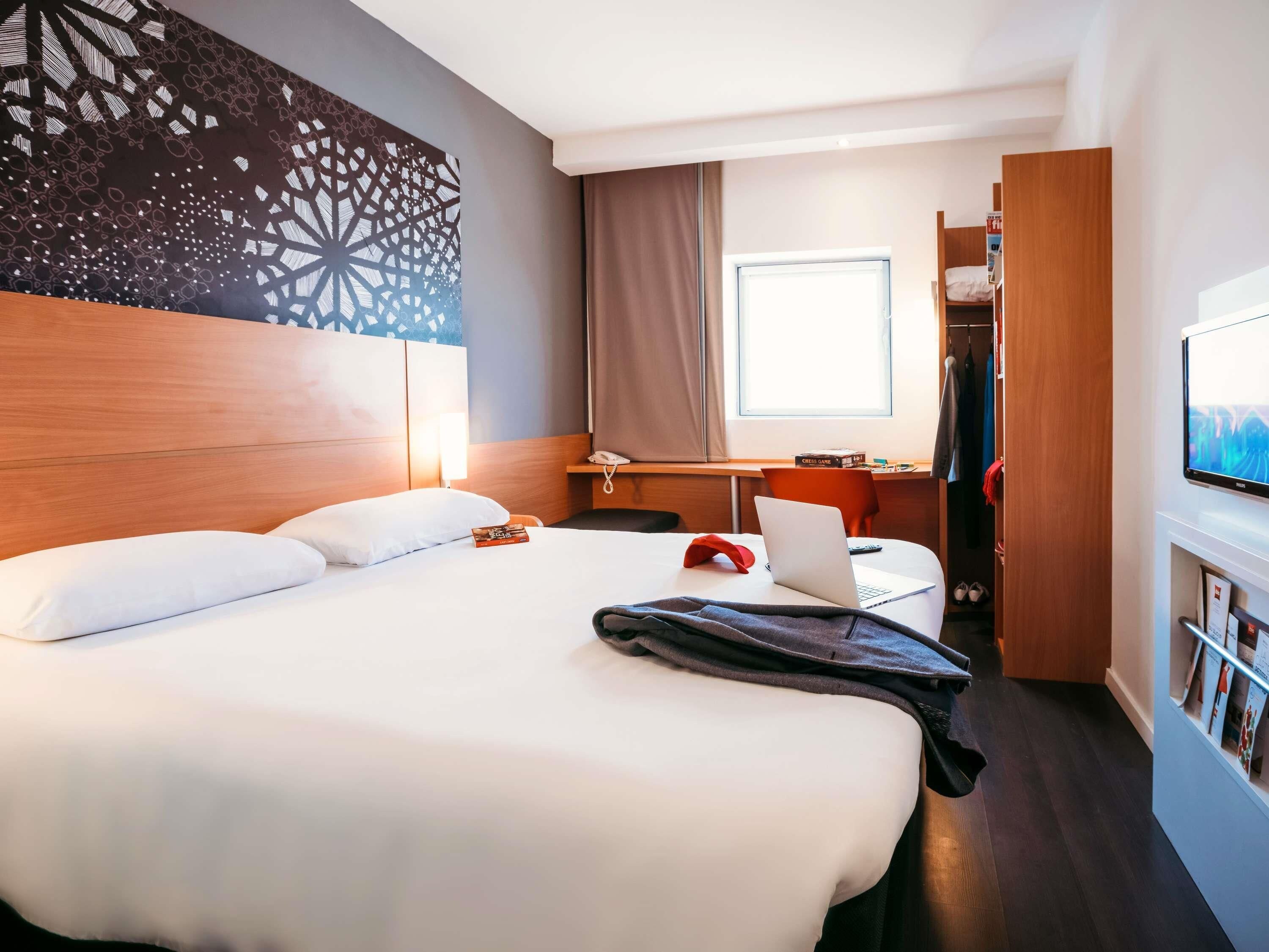 Une chambre d’hôtel avec un grand lit, un bureau avec un ordinateur portable, une télévision et une armoire.