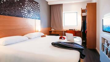 A hotel room with a large bed, a desk with a laptop, a television, and a wardrobe.