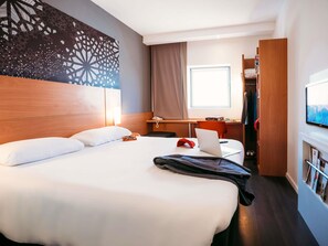 Une chambre d’hôtel avec un grand lit, un bureau avec un ordinateur portable, une télévision et une armoire.