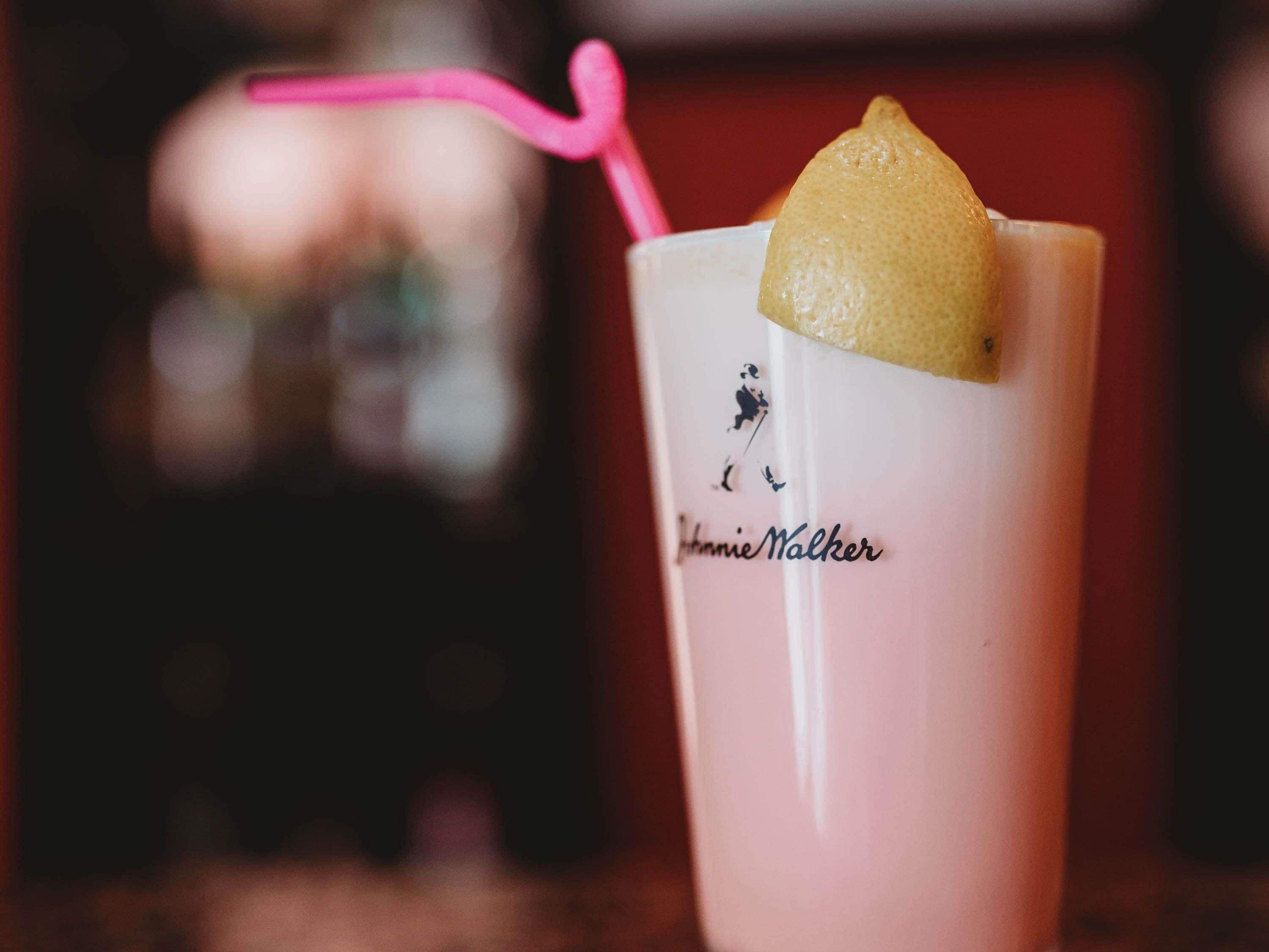 Un vaso con pajita rosa y una rodaja de limón, con la etiqueta 'Johnnie Walker'.
