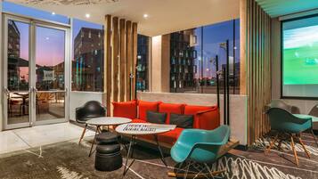 Un interior moderno con un sofá rojo, sillas color turquesa, una mesita y vistas a la ciudad a través de amplios ventanales.