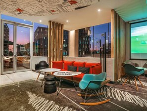Ein modernes Interieur mit einem roten Sofa, blaugrünen Sesseln, einem kleinen Tisch und Stadtblick durch große Fenster.