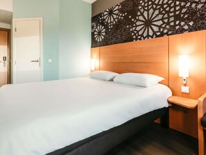 Una habitación de hotel con una cama, dos mesitas de noche, una pared con diseño geométrico y una puerta.