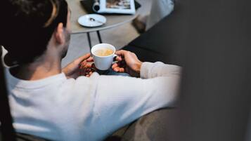 A person holding a cup of coffee, seated at a small round table with a book and a plate.