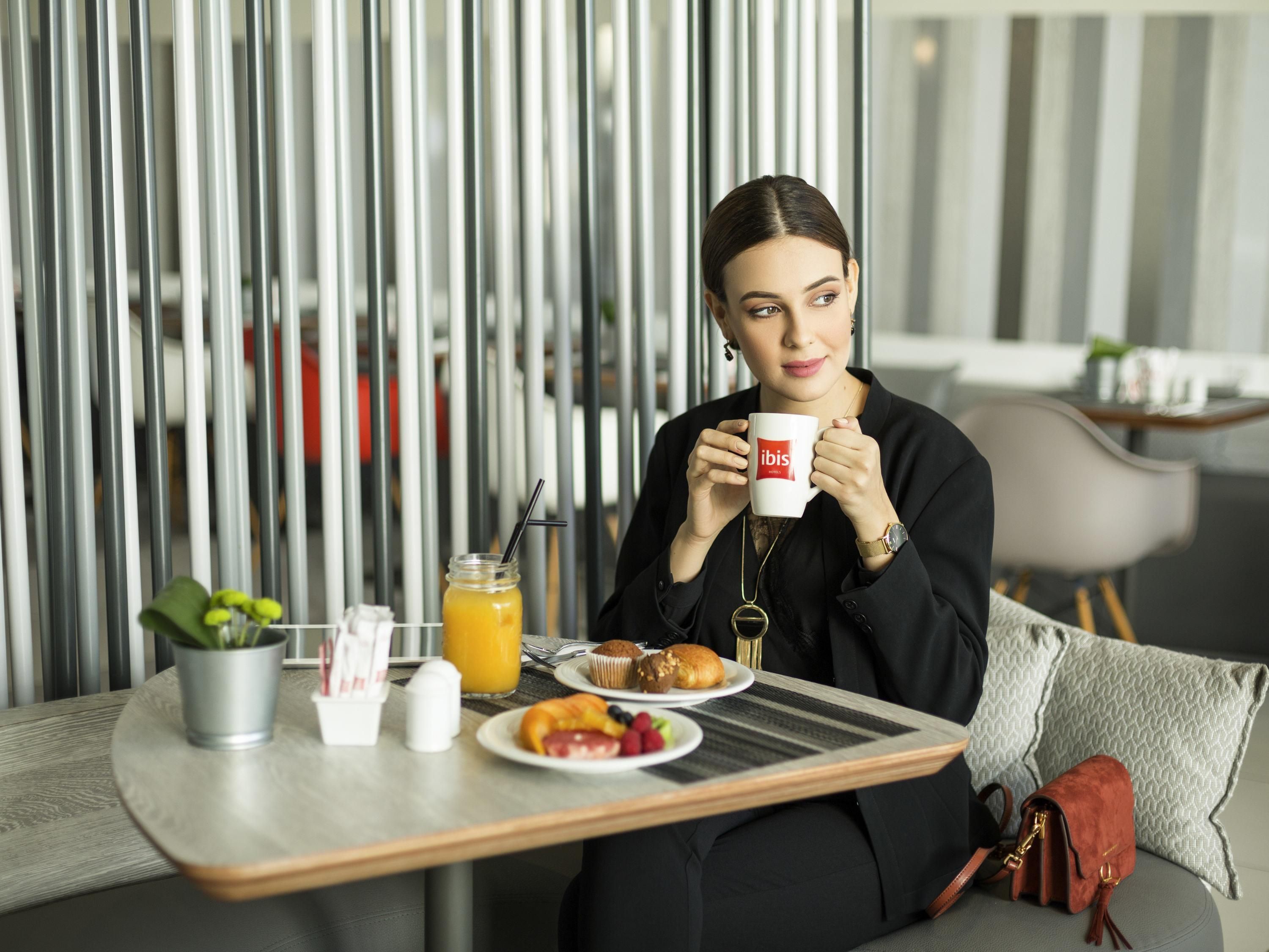 A person sitting at a table with a tray containing food and a drink, in a modern interior with vertical blinds.