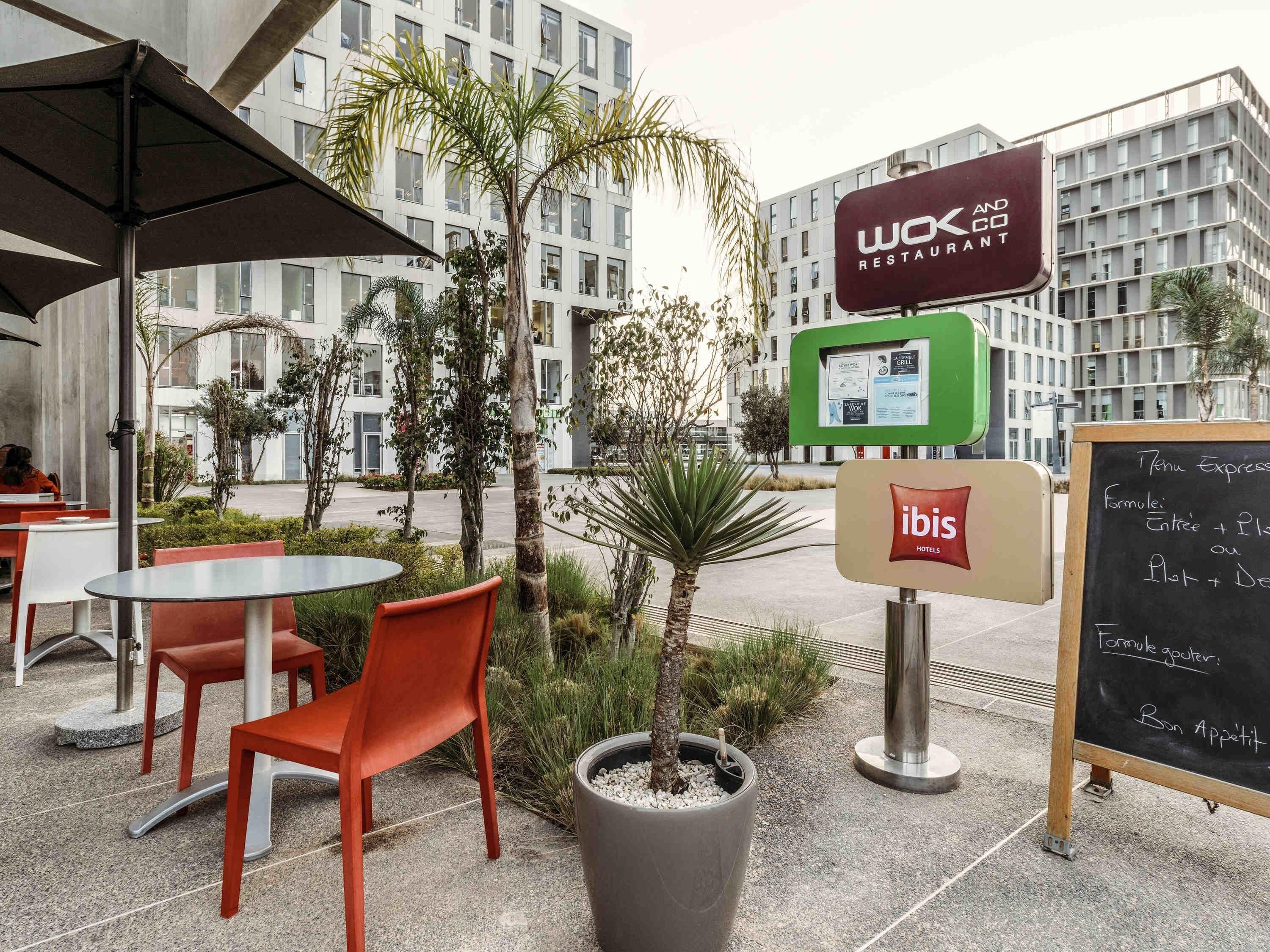 Een terras met rode stoelen en tafels, een bord met 'Wox and Co Restaurant' en een menukaart op een schoolbord.
