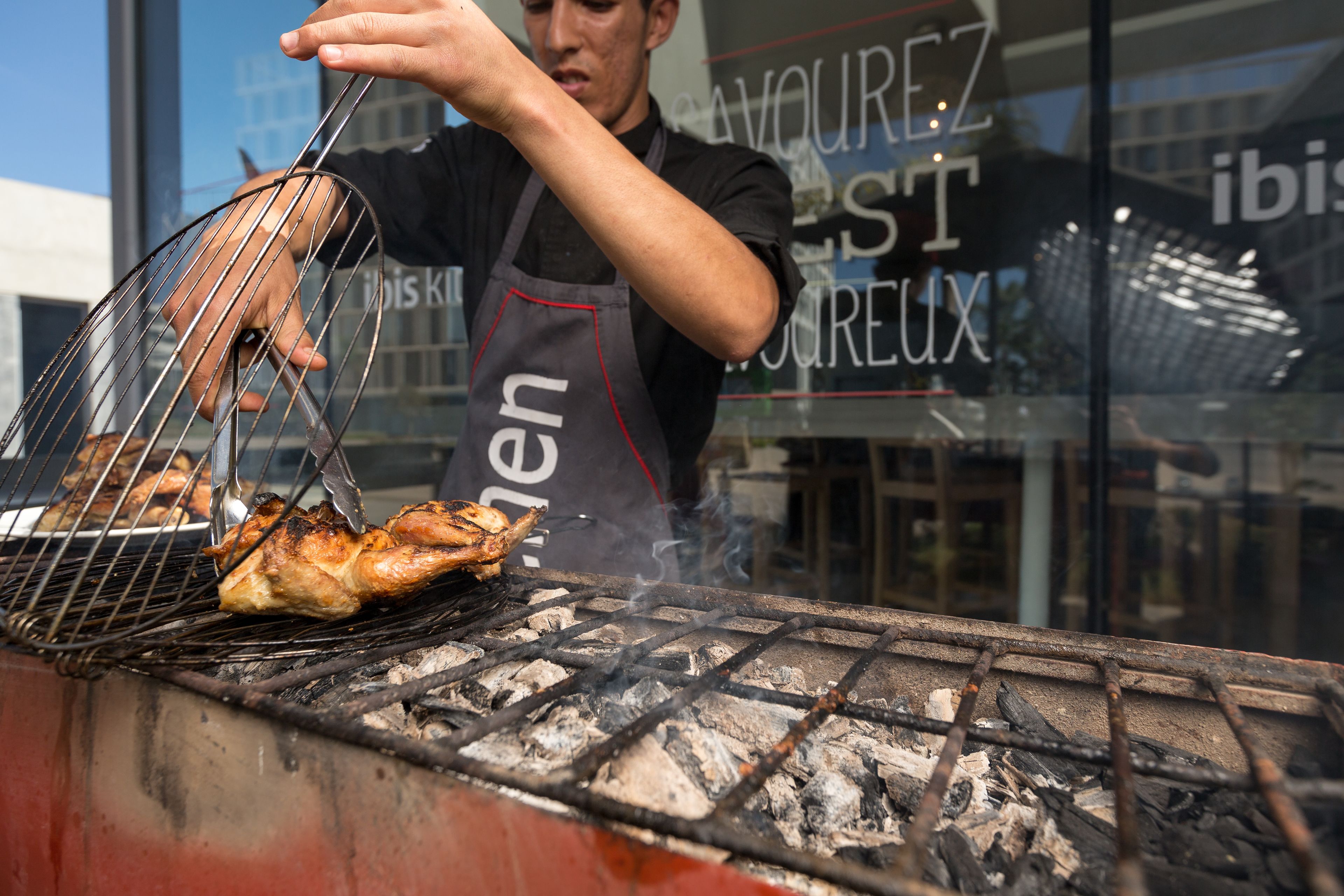 A person grilling chicken on an outdoor grill with visible charcoal and a metal rack.