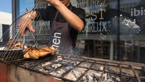 Una persona asando pollo en una parrilla al aire libre, con carbón a la vista y una rejilla metálica.