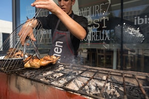 Iemand bereidt kip op een buitenbarbecue, met zichtbaar houtskool en een metalen rooster.