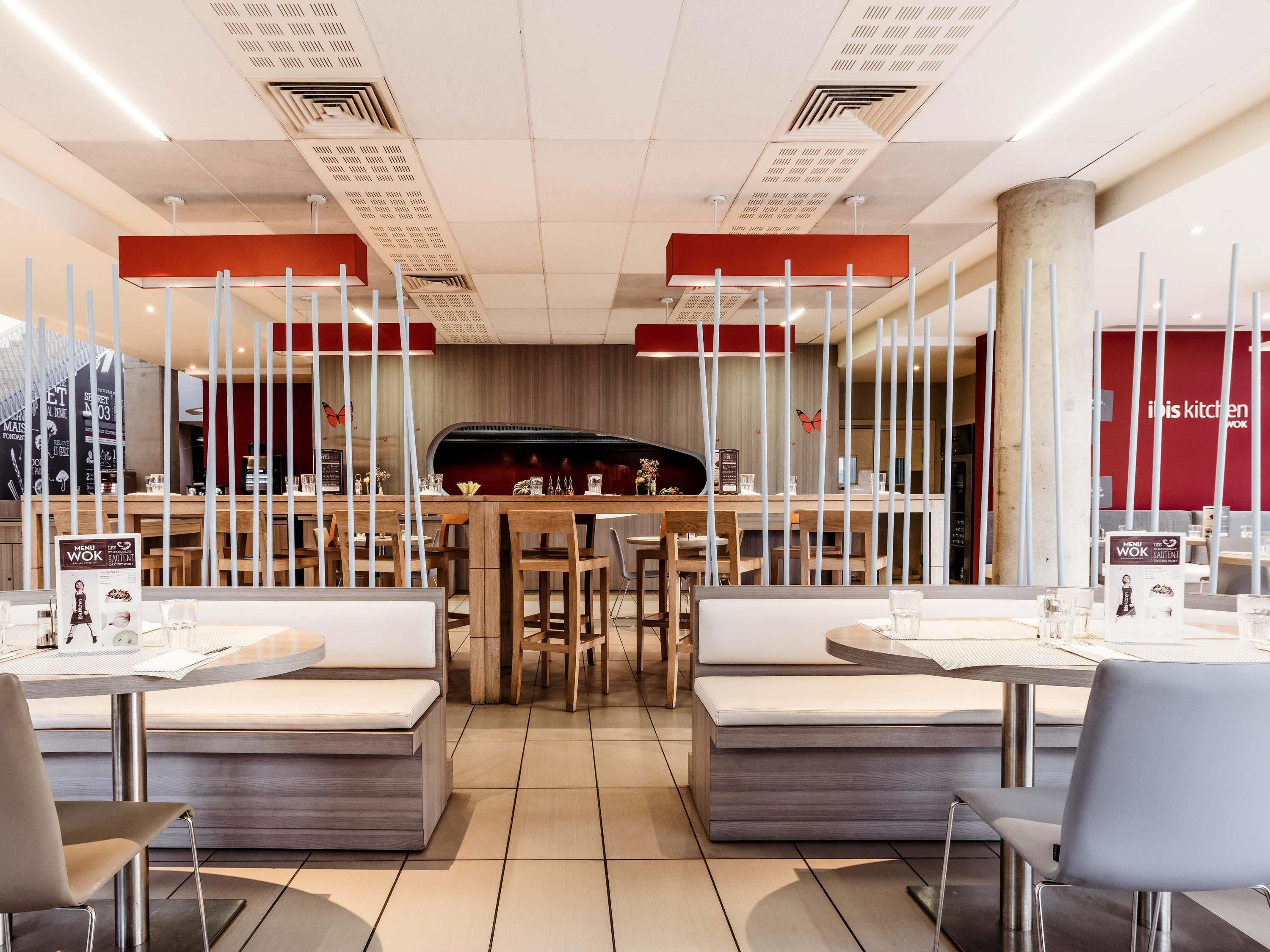 Un intérieur de restaurant moderne avec des tables et des bancs en bois, un bar central et un présentoir pour afficher le menu.