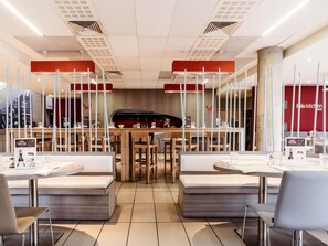 A modern restaurant interior with wooden tables and benches, a central bar area, and a menu display. - Ibis Casablanca Nearshore (Casablanca)