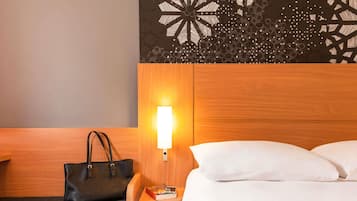 A hotel room with a wooden headboard, a bedside lamp, a black leather bag, a book, and a white bed.