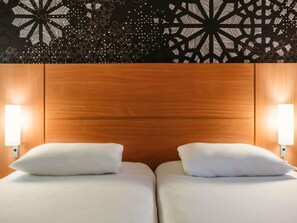 Ein Hotelzimmer mit einem Holzkopfteil, zwei Betten mit weißen Laken und Wandlampen.
