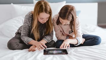 Deux personnes sont assises sur un lit, une tablette est posée devant elles.