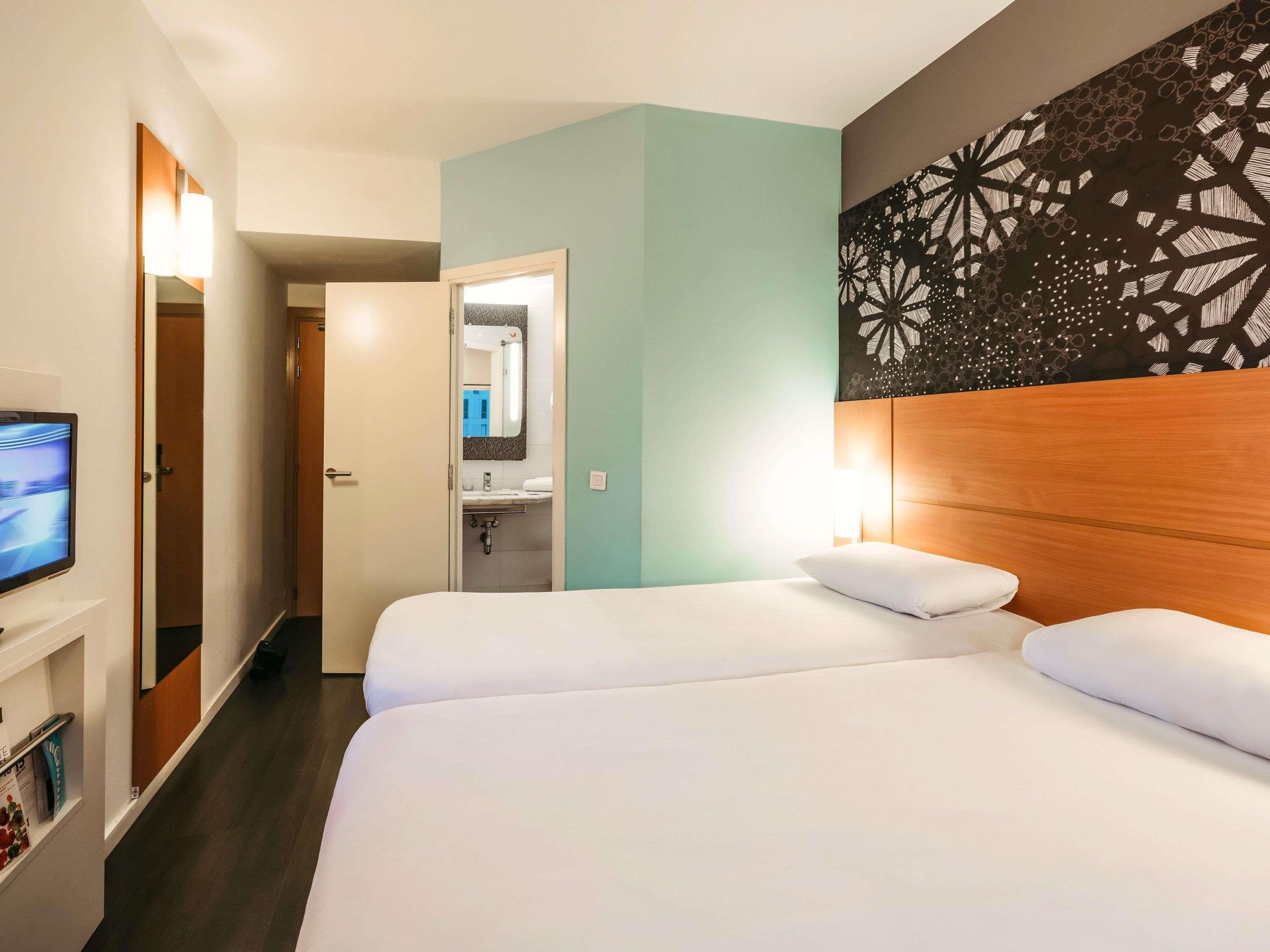Ett hotellrum med en säng, en TV, ett badrum och en dekorativ vägg.