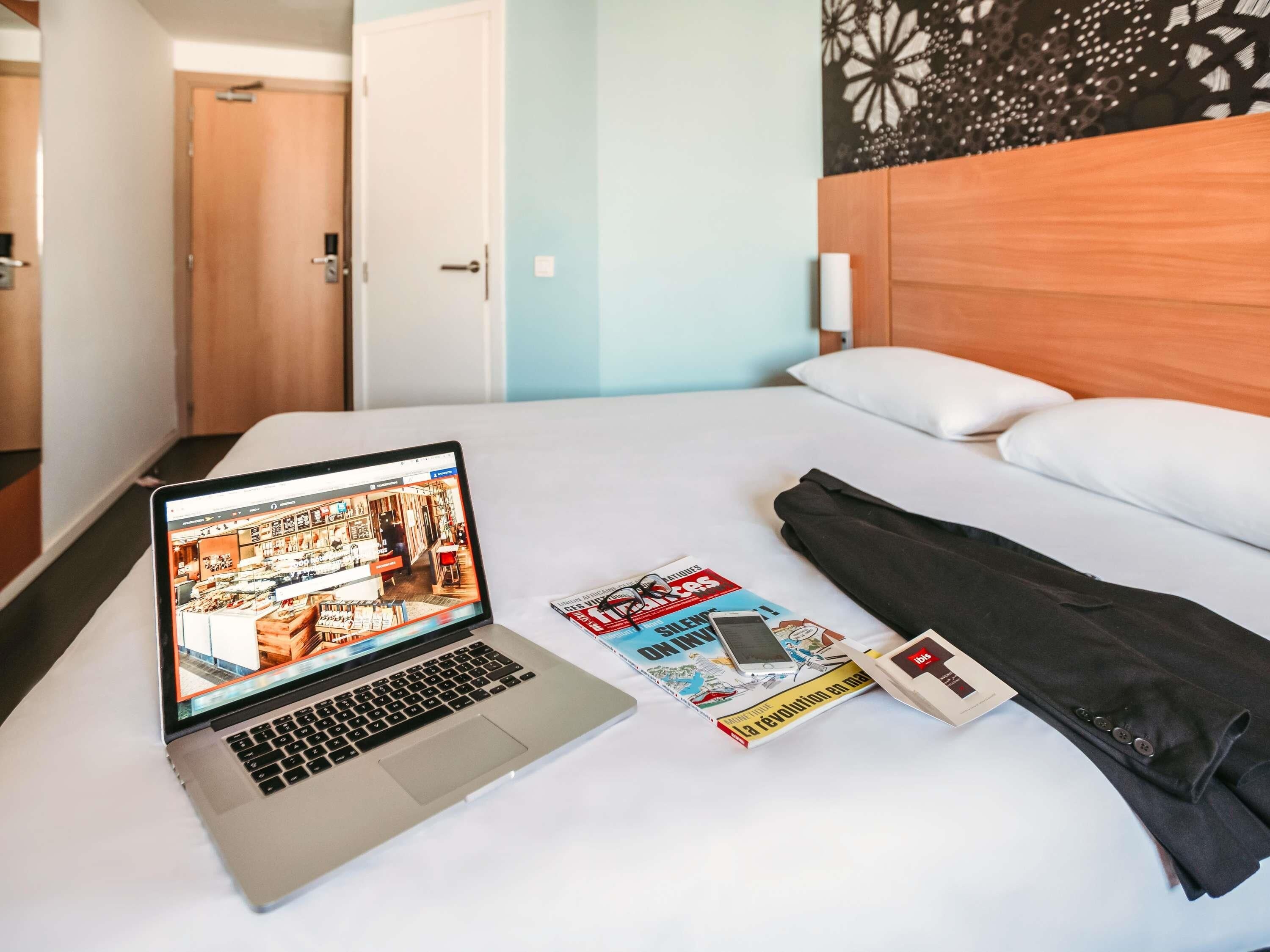 Ein Hotelzimmer mit einem Bett, einem Laptop auf dem Bett, einer Zeitschrift, einem Smartphone und einer Hose.